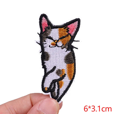 Embroidered patch of a cat's face held between fingers on a white background