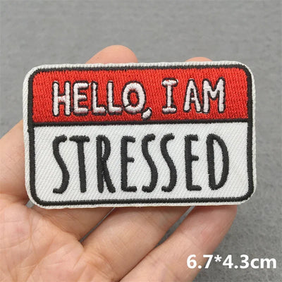 Embroidered patch with 'Hello I am stressed' text held in a hand against a gray background