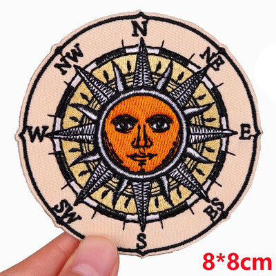 Circular patch with sun and compass design held by a hand, size 8x8cm.