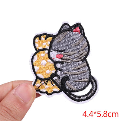 Embroidered patch of a cat and polka dot dress held by a hand on a white background.