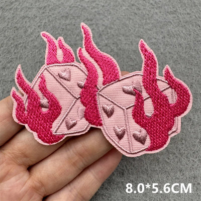 Pink embroidered patches with flame design held by a hand on a gray background