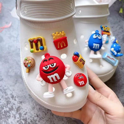 White shoe with colorful M&M's themed shoe charms on a gray surface.