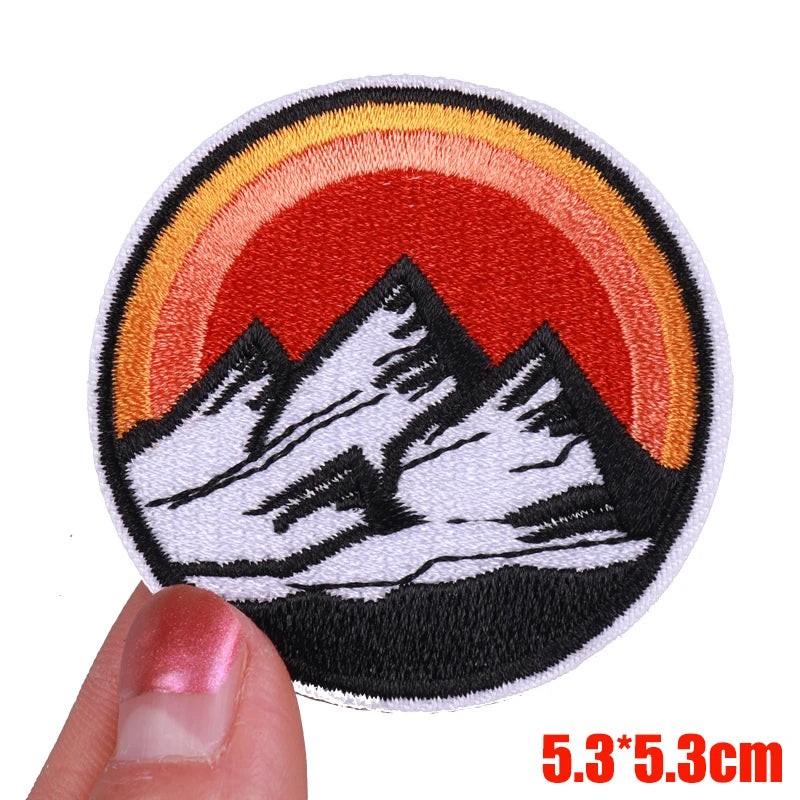 Embroidered patch with mountain design and sunset, held by a hand.