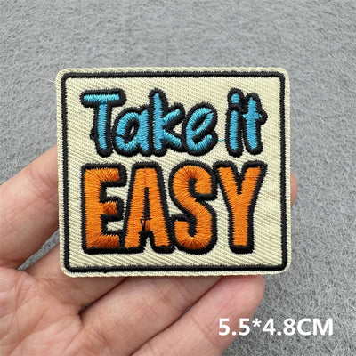 Embroidered patch with 'Take it EASY' text held in a hand against a gray background
