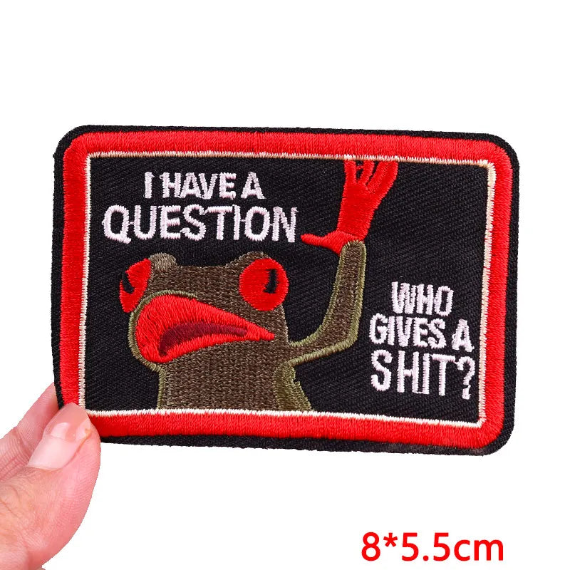 Embroidered patch with a cartoon character and text, held by a hand on a white background.