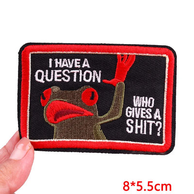 Embroidered patch with a cartoon character and text, held by a hand on a white background.