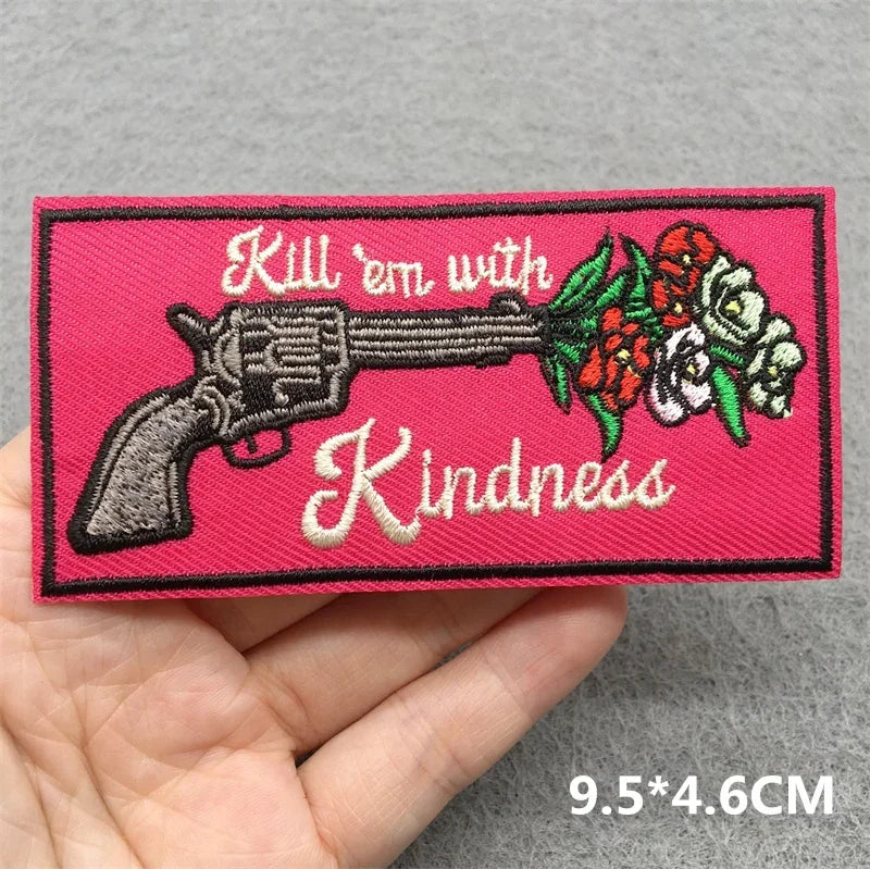 Patch with a gun and flowers design on a pink background, held in a hand.