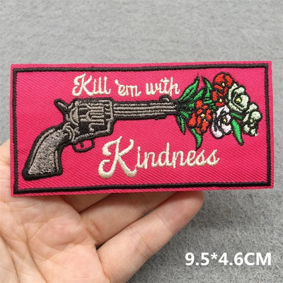Patch with a gun and flowers design on a pink background, held in a hand.