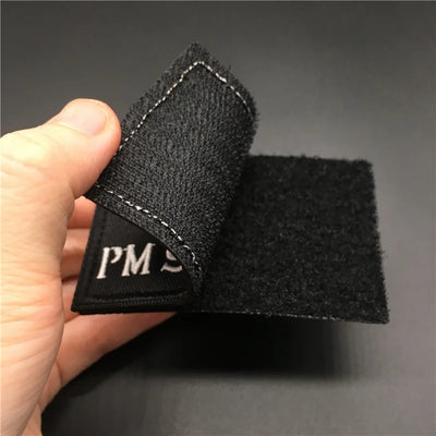 Patch showing its Velcro backing held by a hand against a dark background