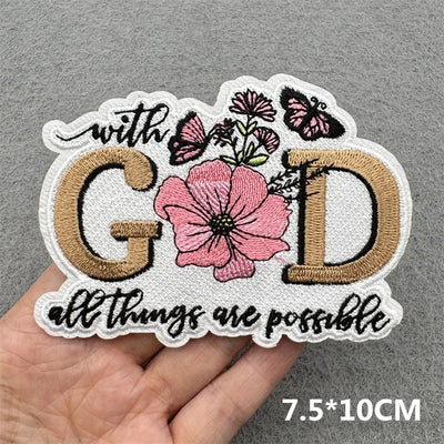 Embroidered patch with 'with GOD all things are possible' text and floral design held by a hand on a gray background.