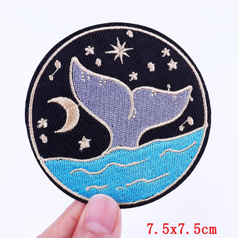 Embroidered patch with whale tail design held by a hand on a white background