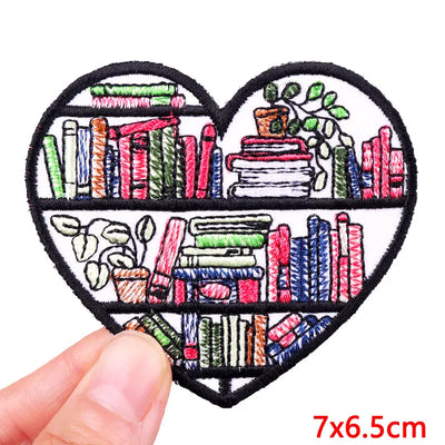 Heart-shaped patch with bookshelf design held by a hand, size 7x6.5cm.