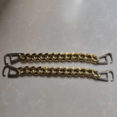 Two gold chain straps with metal hooks for clog on a gray surface