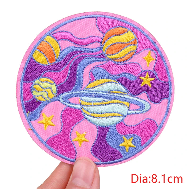 Circular embroidered patch with space design held by a hand, on a white background.