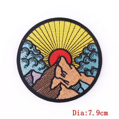 Circular embroidered patch with mountain, sun, and wave design on a white background