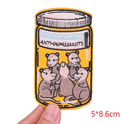 Patch of a jar labeled 'Antidepressants' with cartoon bears on a yellow background, held by a hand.