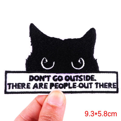 Black cat patch with text 'Don't go outside. There are people out there' held by a hand.