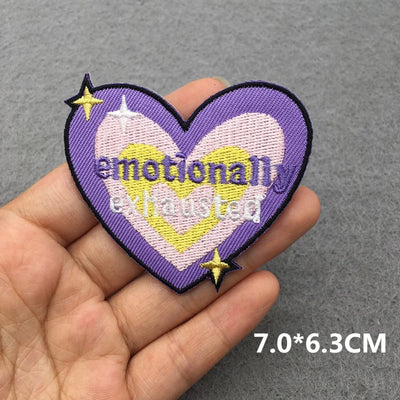 Heart-shaped patch with 'emotional exhausted' text held in a hand against a gray background