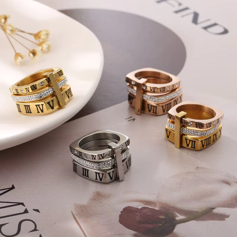 Set of gold, silver, and rose gold rings with Roman numeral design on a magazine background.