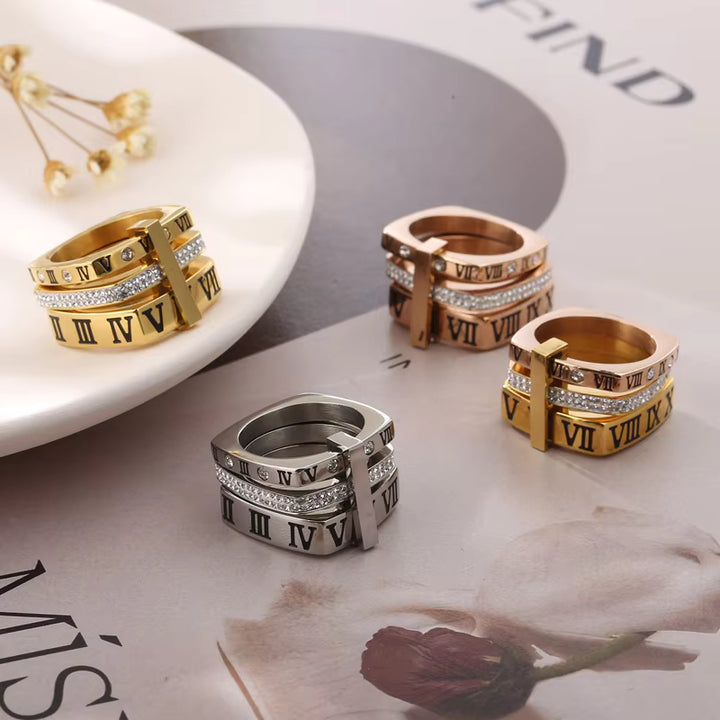 Set of gold, silver, and rose gold rings with Roman numeral design on a magazine background.