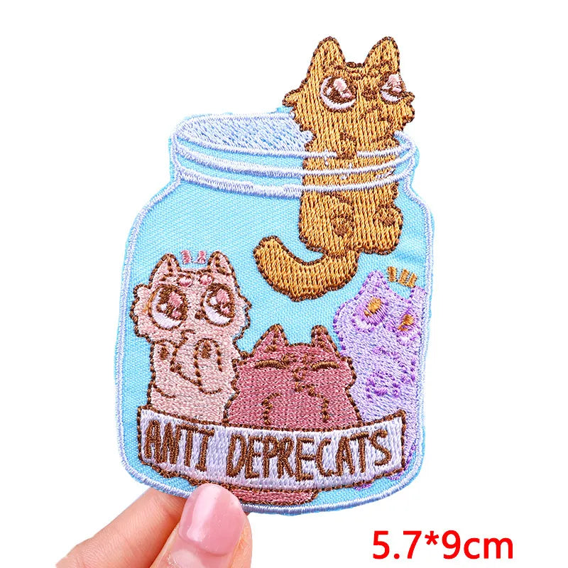 Embroidered patch of cats in a jar with 'ANTI DEPRECATS' text, held by a hand.