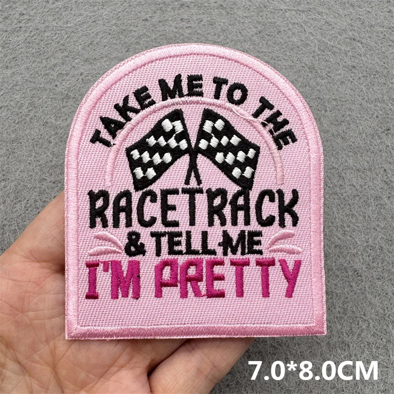 Hand holding a pink black and white embroidered Take Me to the Racetrack and Tell Me I’m Pretty iron-on patch approximately 7x8cm on a gray background