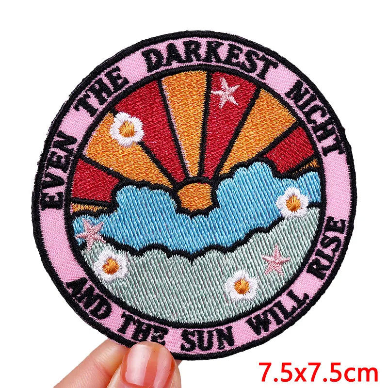 Circular embroidered patch with sunset design and text held by a hand