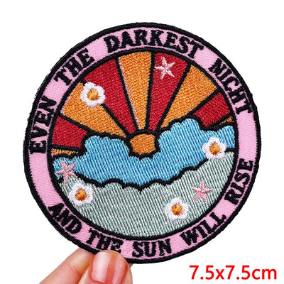 Circular embroidered patch with sunset design and text held by a hand