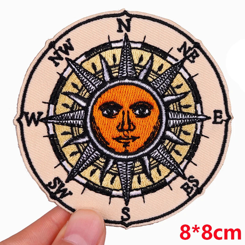 Circular patch with sun and compass design held by a hand, size 8x8cm.