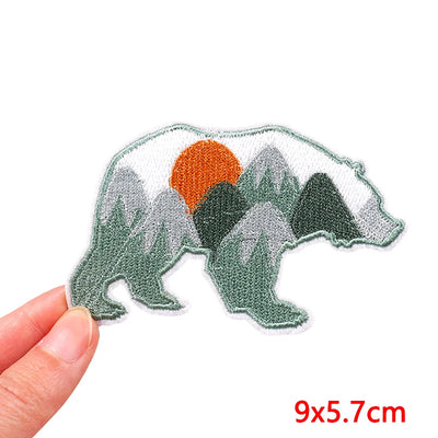 Polar bear patch with mountain and sun design held by a hand, size 9x5.7cm.
