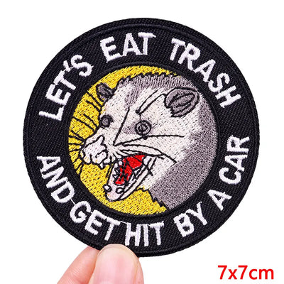 Circular patch with a rat illustration and text 'Let's eat trash and get hit by a car' held by a hand.