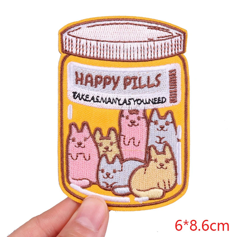 Embroidered patch with cartoon cats in a jar labeled 'Happy Pills' held by a hand.