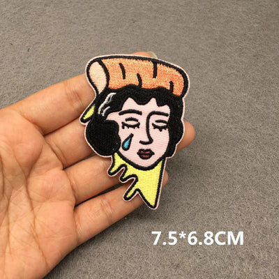 Embroidered patch of a stylized face held by a hand on a gray background