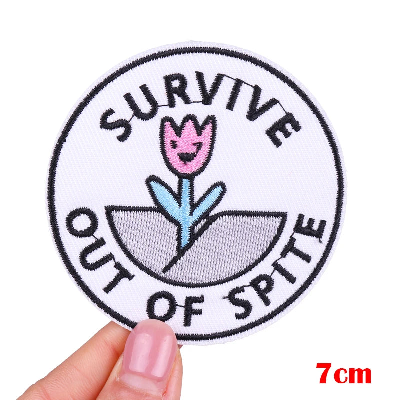 Circular patch with text 'SURVIVE OUT OF SPITE' held by a hand, on a white background.