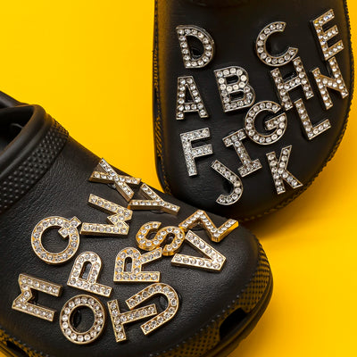 Black clogs with rhinestone letters shoe charms on a yellow background