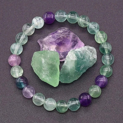 Beaded bracelet with green and purple stones on a dark surface with crystals.