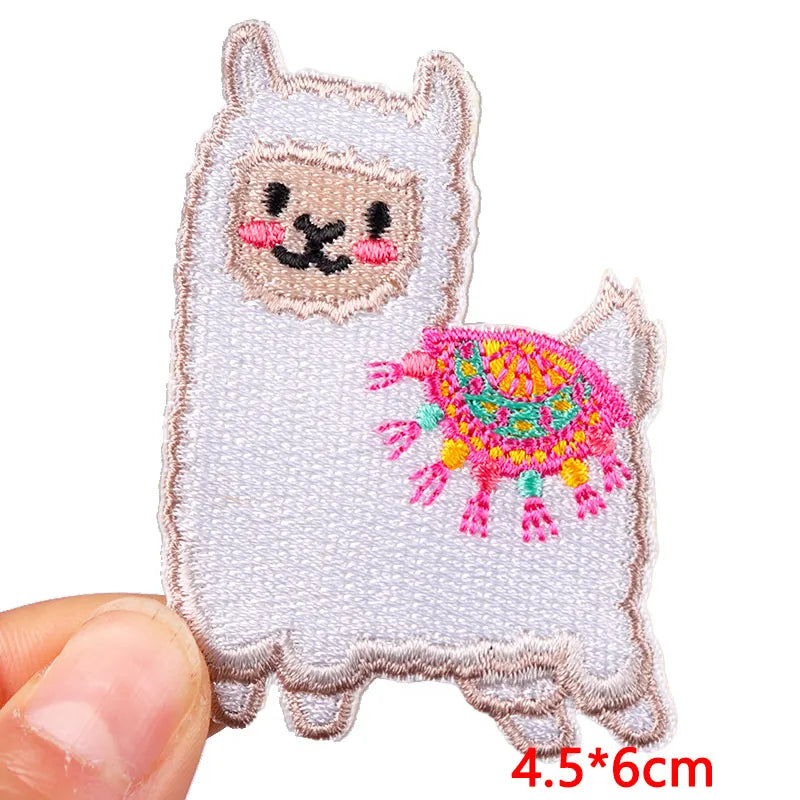 Embroidered patch of a llama with colorful details held by a hand on a white background.