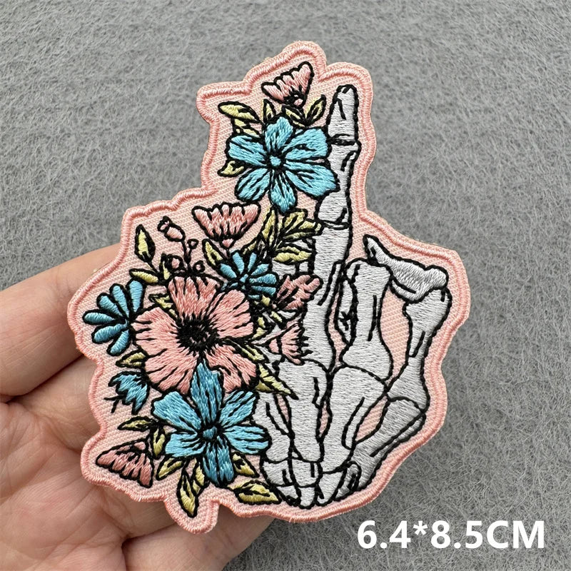Decorative patch with floral and skeleton design held by a hand on a gray background