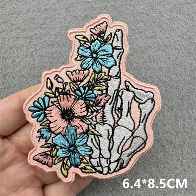 Decorative patch with floral and skeleton design held by a hand on a gray background
