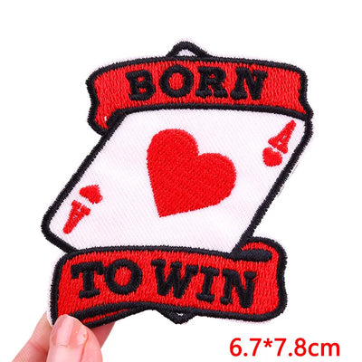 Embroidered patch with a heart design and text 'BORN TO WIN' held by a hand.