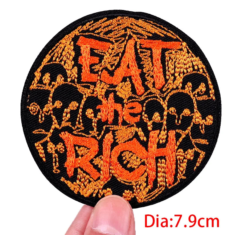 Circular patch with 'EAT THE RICH' text in orange on a black background, held by a hand.