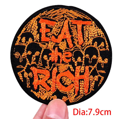 Circular patch with 'EAT THE RICH' text in orange on a black background, held by a hand.