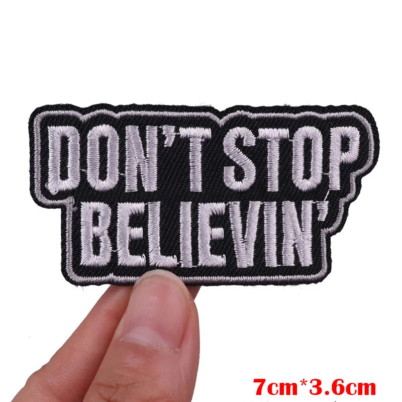 Embroidered patch with 'DON'T STOP BELIEVING' text held by a hand on a white background.