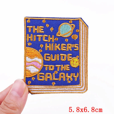 Embroidered patch of 'The Hitchhiker's Guide to the Galaxy' book held by a hand.