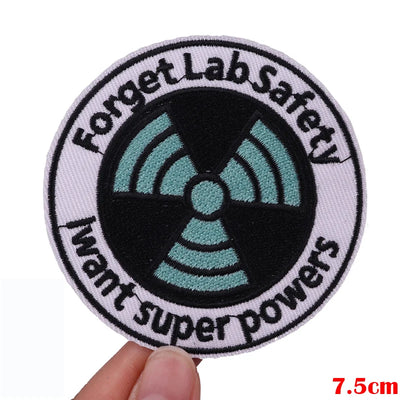 Patch with 'Forget Lab Safety, I want super powers' text and radiation symbol held by a hand.