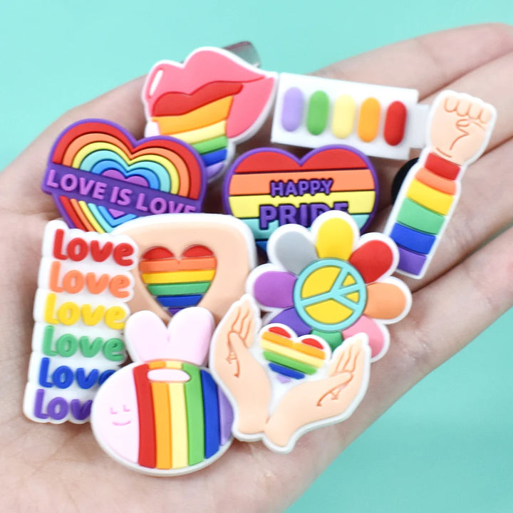 Collection of colorful Pride-themed shoe charms held in a hand against a light blue background.