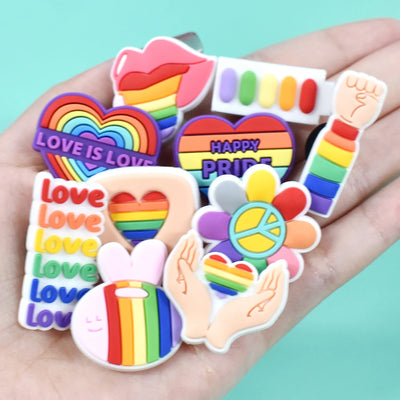 Collection of colorful Pride-themed shoe charms held in a hand against a light blue background.