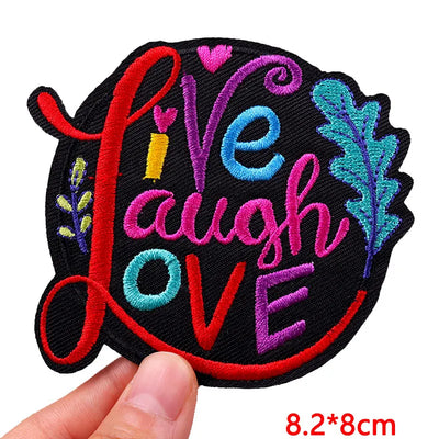 Embroidered patch with 'Live Laugh Love' text held by a hand, on a white background.