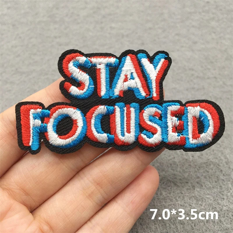 Embroidered patch with 'STAY FOCUSED' text held in a hand against a gray background