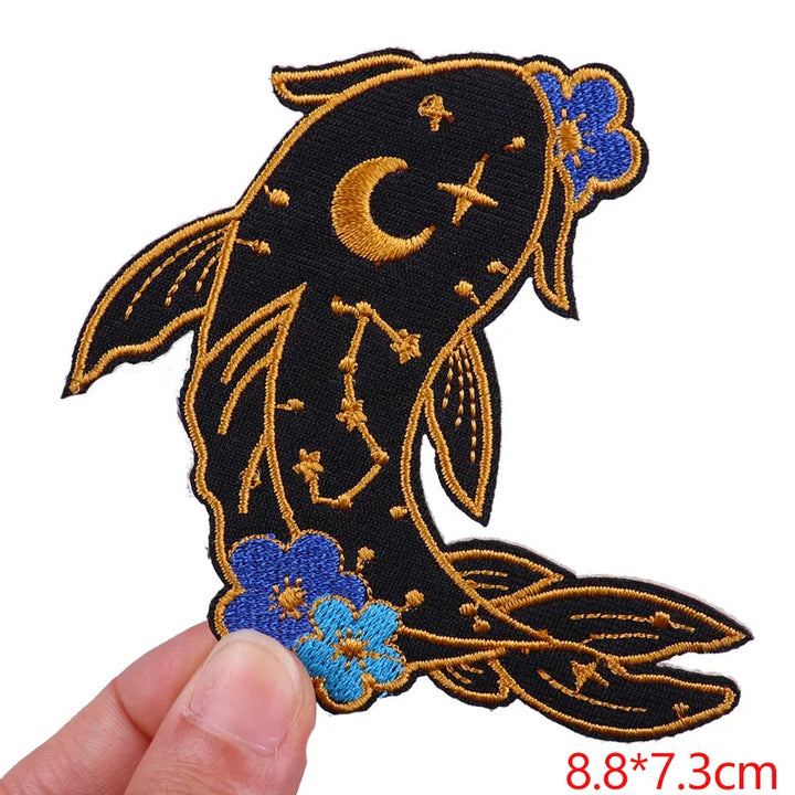 Embroidered patch of a fish with celestial designs held by a hand on a white background.